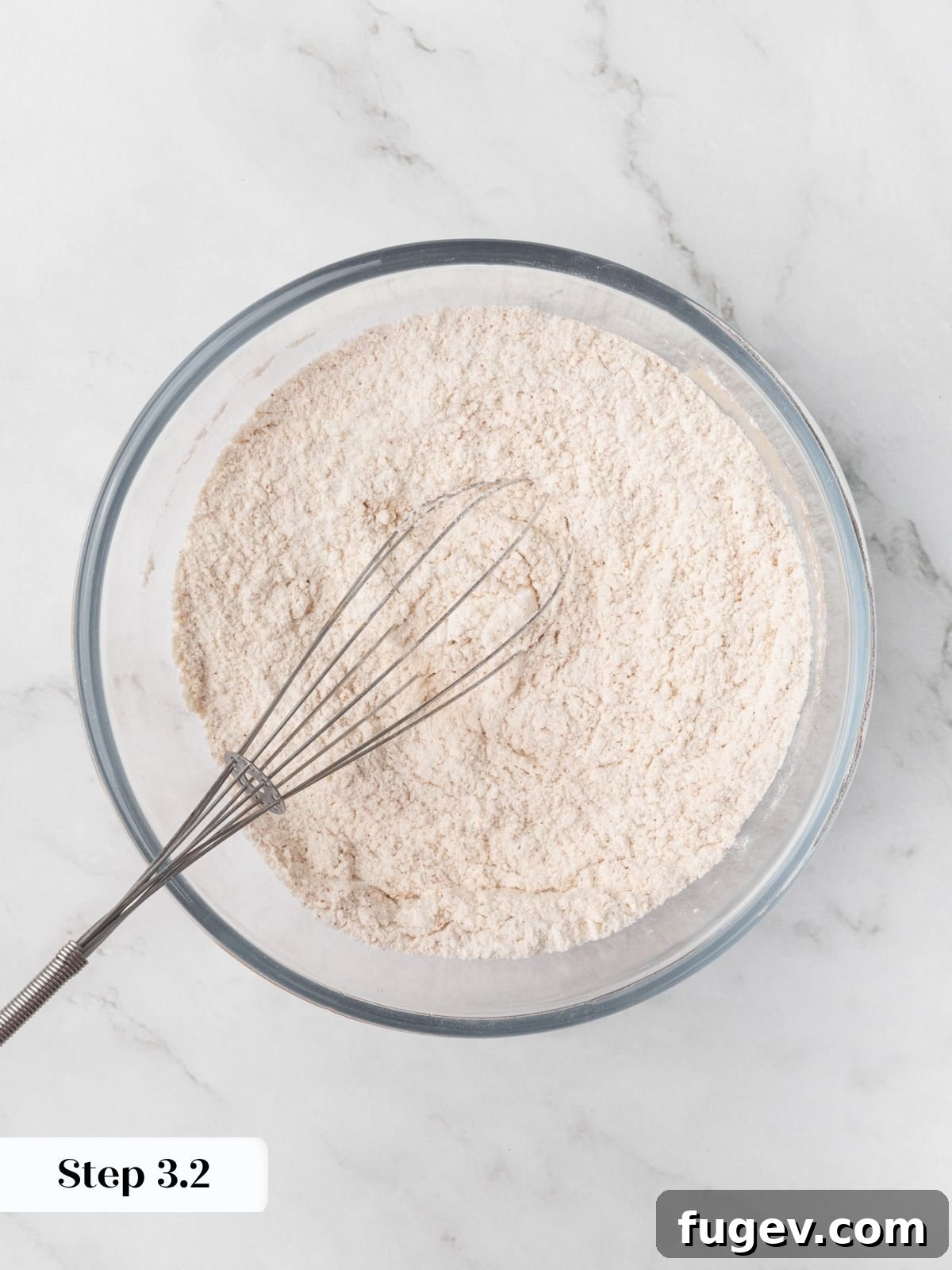 Pale tan dry mixture flecked with cinnamon evenly whisked together in a clear glass bowl.