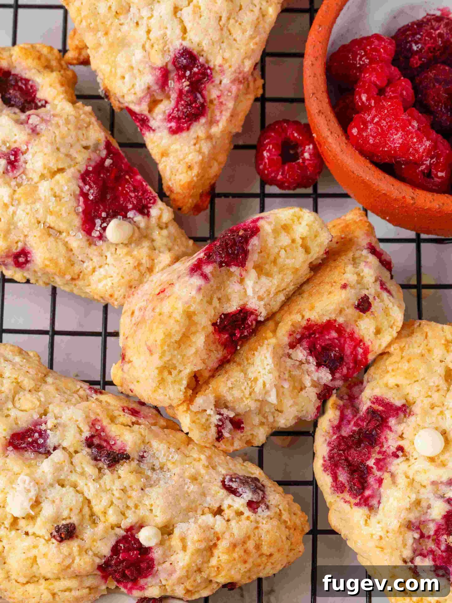 White Chocolate Raspberry Bliss Scones 2 A batch of freshly baked raspberry white chocolate scones cooling on a wire rack next to a small bowl of frozen raspberries.