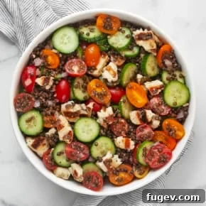 Lentil salad with grilled halloumi, cucumbers and tomatoes in a large bowl.